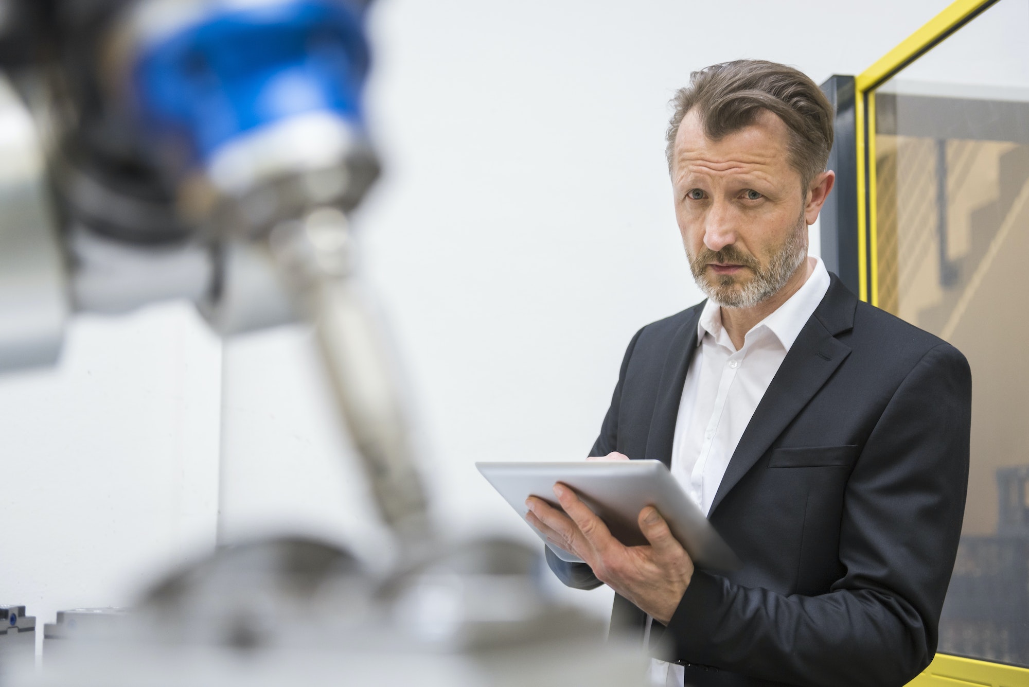 Mature businessman controlling industrial robots with digital tablet