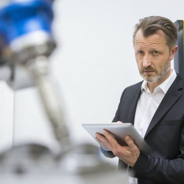 Mature businessman controlling industrial robots with digital tablet