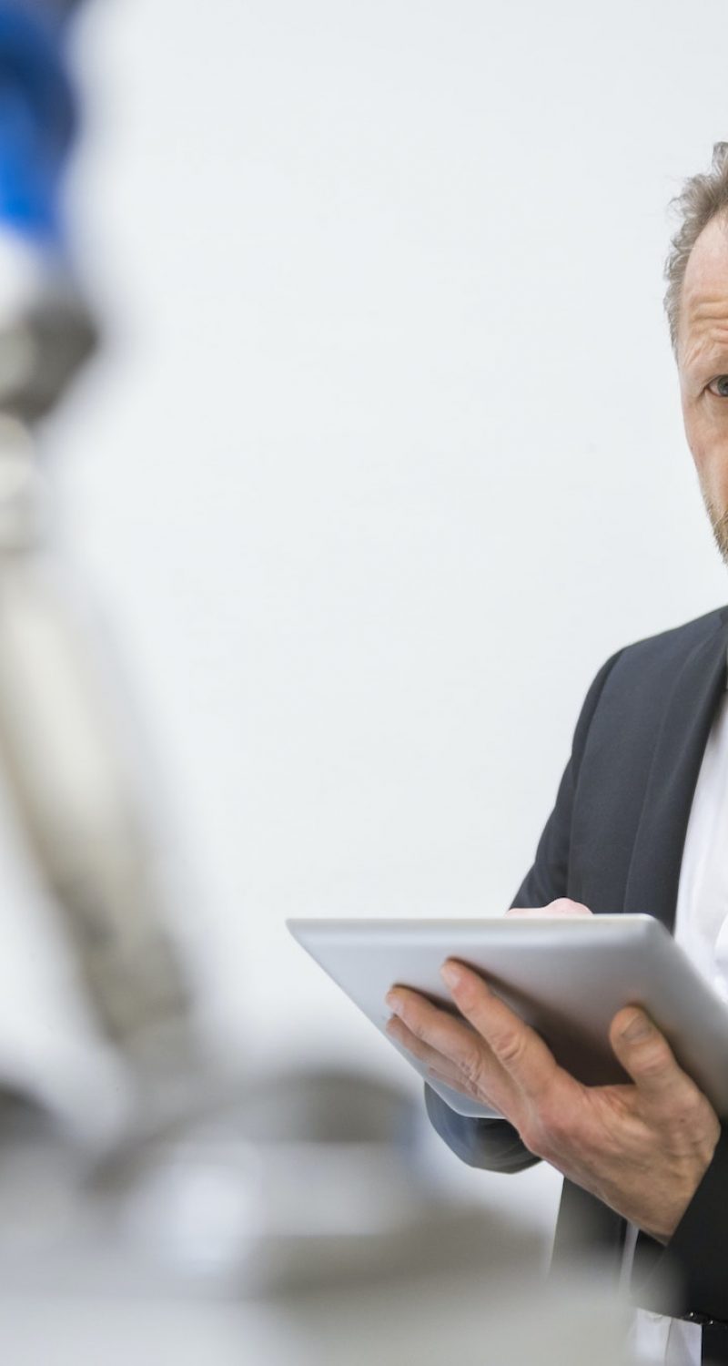 Mature businessman controlling industrial robots with digital tablet