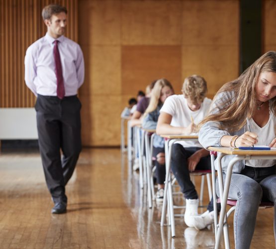 Teenage Students Sitting Examination With Teacher Invigilating